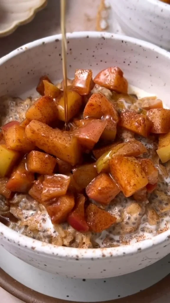 A bowl of apple cinnamon oatmeal topped with fresh apple slices and cinnamon.