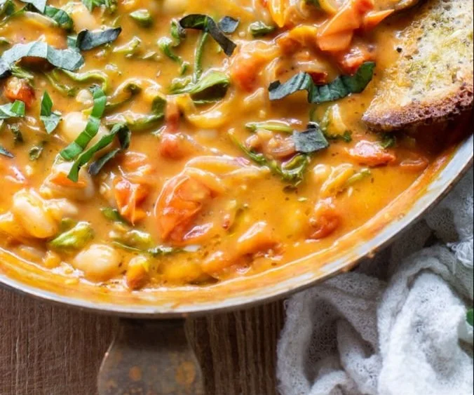 Delicious creamy vegan tomato white bean stew in a bowl garnished with herbs