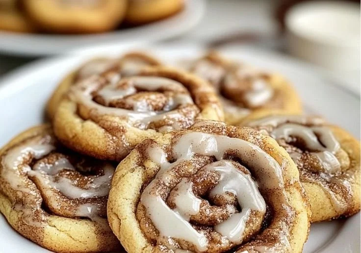 Freshly baked cinnamon roll cookies drizzled with icing on a baking sheet.