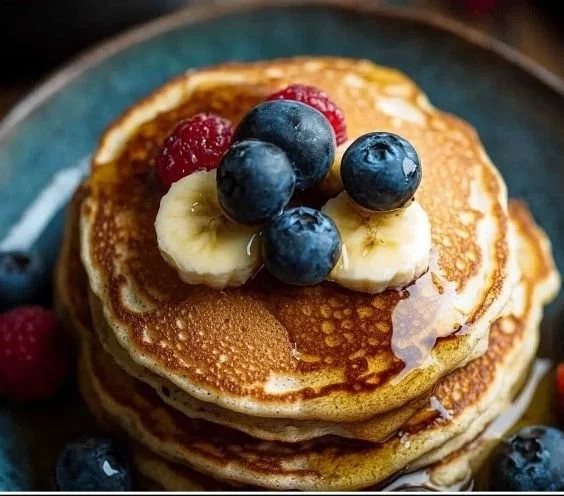 Gluten-free banana pancakes served with fresh fruit and syrup on a plate.