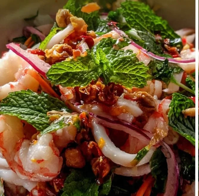 A colorful Vietnamese seafood salad with shrimp, fish, and fresh herbs on a plate.