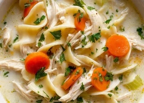 Bowl of creamy chicken noodle soup with vegetables and herbs
