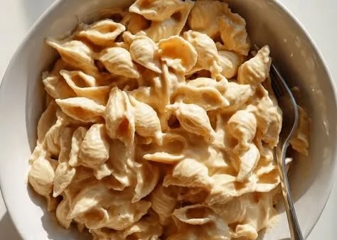 A bowl of creamy hummus pasta topped with fresh herbs and vegetables