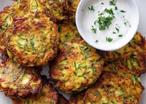 Zucchini and sweet potato fritters on a plate, garnished with herbs.