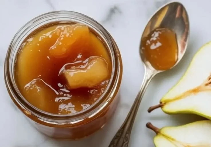 Jar of delicious homemade pear jam on a wooden table with fresh pears.