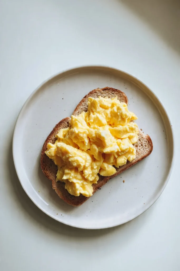 Plate of fluffy scrambled eggs garnished with herbs.